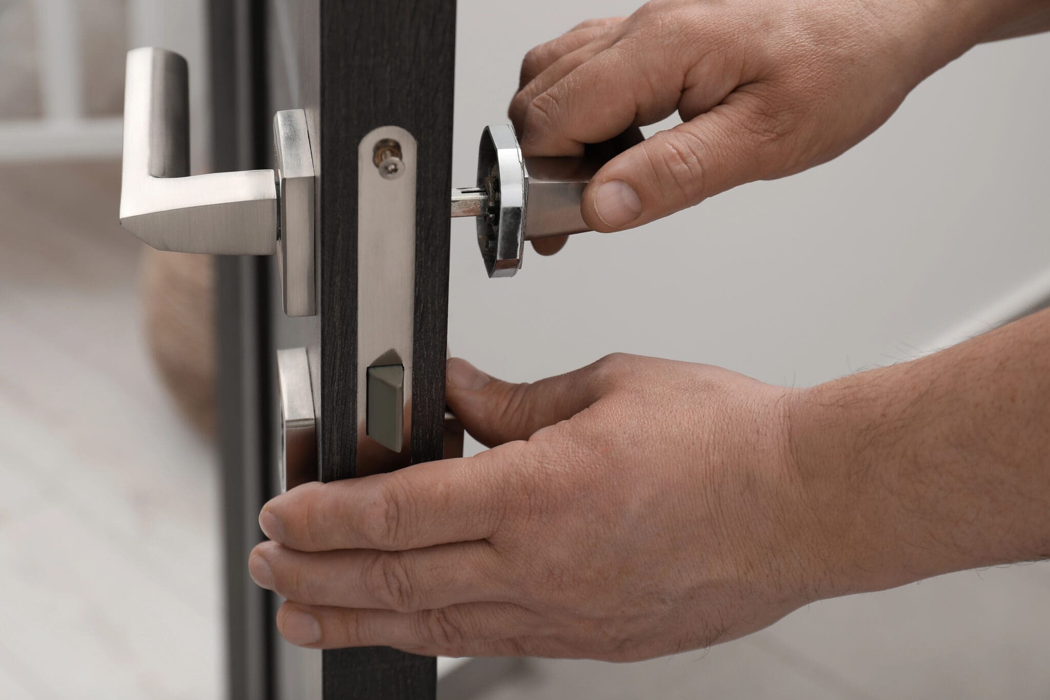 Close-up of a person’s hands installing or repairing a modern door lock with a silver handle, inserting a key into the lock cylinder on a dark-colored door—ideal for glazier services or alongside window repairs.