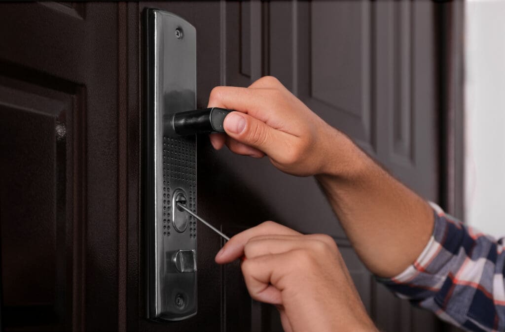 A person uses tools to pick the lock on a metal door, with one hand holding the lockpick and the other turning a tension wrench in the keyhole—demonstrating skills essential for fixing broken locks or handling window repairs.